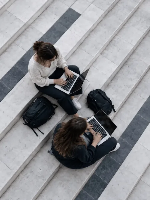 Due studentesse lavorano al laptop sedute su una scalinata in marmo